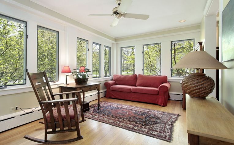 A solarium with an armchair and red loveseat and a rug